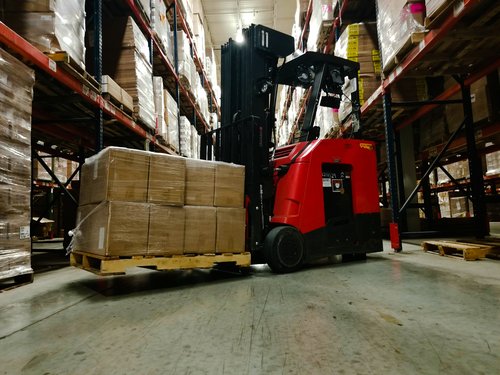 a stand up forklift in a warehouse with a load on forks